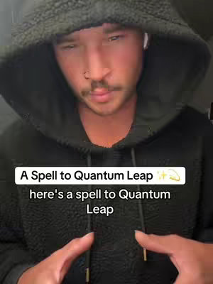 A close-up shot of a man in a black hoodie with text overlays about a spell and quantum leaping. The man has short light brown hair, a slight mustache, and a nose ring. The background is dark and out of focus.