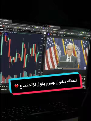 The cover image shows a laptop screen displaying a live video feed on the right section. The feed features a man speaking at a podium with flags of the United States behind him. On the left side of the screen, there's a graph with vertical red and green bars, indicating stock market activity. A colored text bar with the words  "لحظه دخول جيرم باول للإجتماع " appears in the middle, with a broken heart emoji. The screen is set against a dark background, suggesting recording from a desk setup. A keyboard is visible below as well