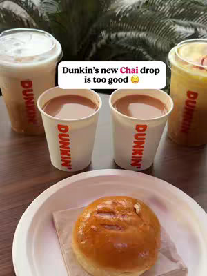 The image showcases a collection of Dunkin' beverages and a pastry. Two cups of a brown drink are centered, flanked by two drinks in clear cups with lids and another with a red and yellow hue. A glazed donut is nestled on a white plate at the bottom.