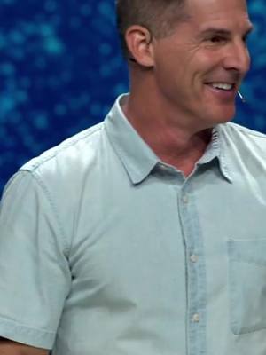 A man in a light blue button-down shirt smiles, slightly turned to his right. The background is a blurry, abstract dark blue with lighter blue highlights.