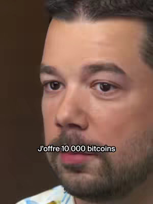 The cover image is a close-up shot of a man's face. The man has short, dark hair and a light complexion. He appears to be speaking, with his lips slightly parted. Text in a white box at the bottom of the image reads, "J'offre 10 000 bitcoins". The background is a blurred, dark brown.