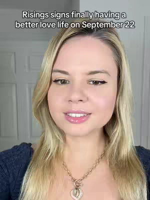 A woman with blonde hair and a dark blue top smiles directly at the camera. Text overlaid at the top reads: "Risings signs finally having a better love life on September 22". The background is blurred, suggesting an indoor setting.