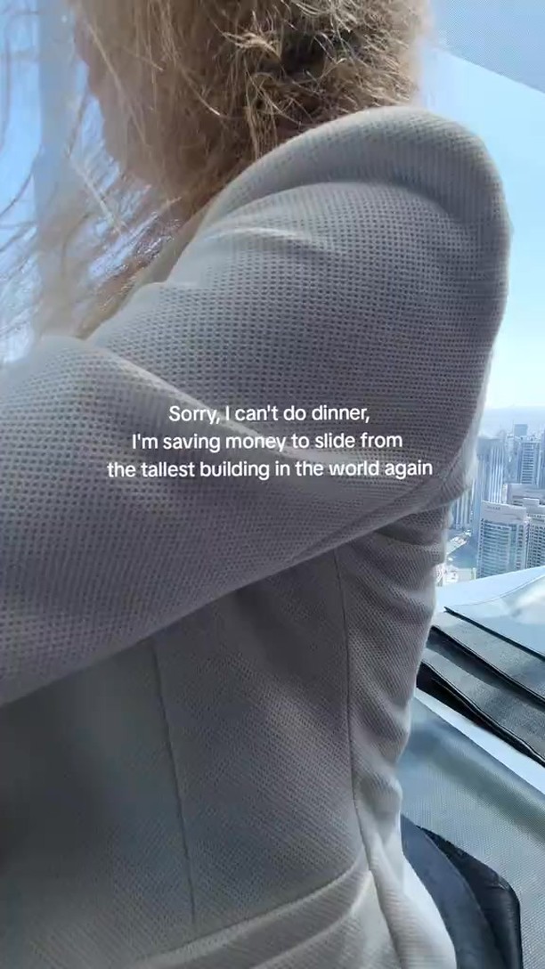 A person is seen from the back in a high-rise building, looking out at a cityscape under a clear sky. The person is wearing a light-colored blazer, and text is overlaid on the image.