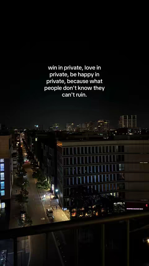 A vertical shot of a nighttime city scene. A dark sky hangs above buildings with illuminated windows, suggesting a cityscape with a road lined by trees. A quote is overlaid with white text.