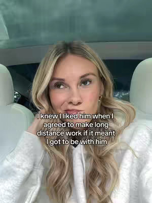 A woman with long blonde hair is sitting in a car, angled towards the camera, and a text overlay appears on the bottom, she is wearing a white hoodie.