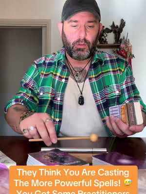 A man with a beard, wearing a black cap and a green plaid shirt, is sitting at a table with tarot cards. The text overlaid on the image is in an orange box.