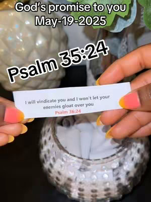 A close-up shot of a person's hands holding a small white paper with a biblical verse while being surrounded by floral and decorative elements.