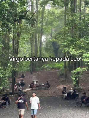 An outdoor scene in a forest with a pathway leading into the distance. The pathway is surrounded by tall trees and lush greenery. There are groups of people around the pathway and at various points sitting on chairs or on picnic blankets. The text 'Virgo bertanya kepada Leo' overlays on to the image.