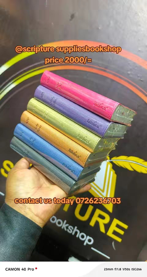 A hand holding a stack of Bibles with different colored covers. The background is dark with blurred circular patterns and text. Text overlays highlight the store name, price, and contact information.