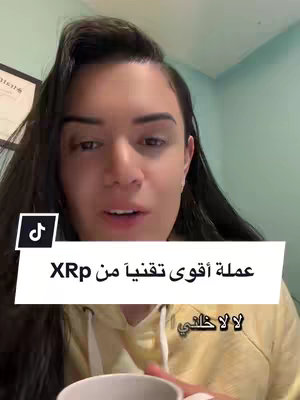 A young woman with long dark hair is centered in the frame, positioned in front of a light green wall, with a framed document visible on the left. She is wearing a yellow hoodie and holding a white cup. A text overlay with a white background and black outlined text covers the lower part of the screen.