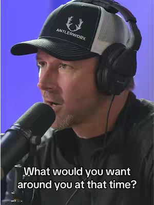 A man wearing a baseball cap and headphones speaks into a microphone, set against a blurred purple background. Text overlayed at the bottom asks a question.
