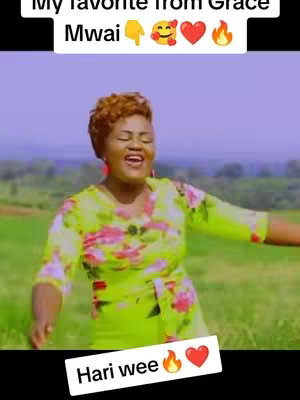 The cover image features a woman with short, curly brown hair, positioned center-frame. She's wearing a yellow floral top, smiling, and singing with her arms outstretched, suggesting a performance or expression of joy. The background is a blurred green field under a sky filled with shades of blue. Text overlaid at the top says, "My favorite from Grace Mwai", followed by emojis: a downward pointing hand, a smiley face, a heart, and flames. Towards the bottom, text appears on a white block saying 'Hari wee', with flames and a heart.