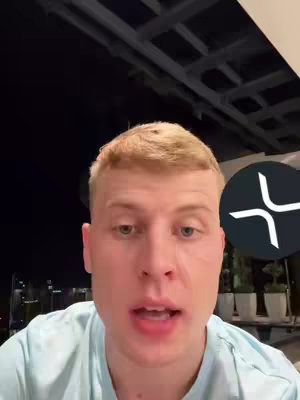 A man with short blond hair speaks directly to the camera, set against a background that appears to be outdoors at night. To the right, there's a circular logo featuring a stylized symbol.