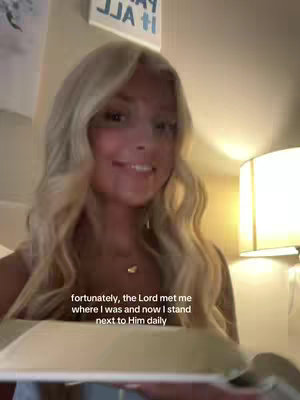 A selfie-style video cover image. A woman with long, wavy blonde hair is smiling at the camera. The background is dimly lit, with a sign in the upper-left corner reading, "IT ALL". Text overlays are present at the bottom of the screen.