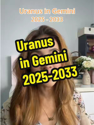 The image is a selfie-style video cover featuring a woman with long, light brown hair, facing the camera directly. She is wearing a patterned top and a necklace. Overlaid on her face and chest are the words "Uranus in Gemini 2025-2033" in a yellow, bold font with a black outline; these words partially obscure her face. Above the main text, in smaller text is "Uranus in Gemini 2025 -2033". The background is slightly blurred, with hints of a room setting including a white wall.