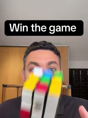 A man with blue eyes is the central figure, blurred while holding a colorful cube puzzle in front of his face. The text overlayed reads 'Win the game'.