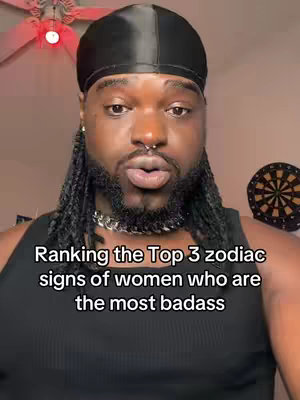 A man with a beard, black durag, chain jewelry, and a nose ring is centered in the frame, looking directly at the viewer. Overlaid text ranks zodiac signs. A dartboard is visible in the blurred background.