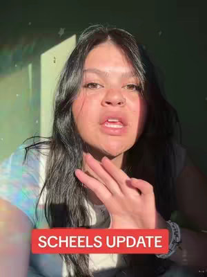 A woman is centered in the frame, appearing to speak. Her dark hair is styled down. A red rectangular box at the bottom of the frame displays the text 'SCHEEELS UPDATE'. The background is a mix of green and includes some light streaks at the top.