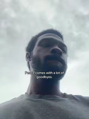 A man with a beard is seen from the chest up, set against a partly cloudy sky. Text overlaid near the center reads a quote. The man is wearing a grey t-shirt.