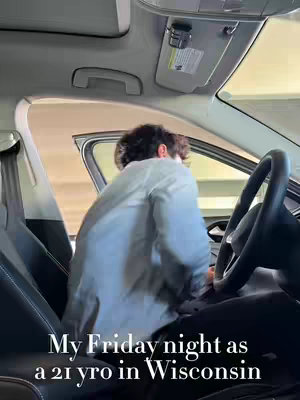 The image shows the interior of a car, with a person in a light-colored shirt facing away from the camera, getting into the driver's seat. The car interior is black and gray, with a visible steering wheel and window frame. The text overlay reads 'My Friday night as a 21 yro in Wisconsin'.