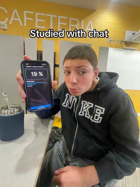 A young man is shown holding up a smartphone. The phone's screen displays a test result of 19%. The man is looking at the camera with a concerned expression. The background is the interior of a school cafeteria with yellow walls and the word "CAFETERIA" visible.