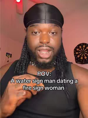 A person with dark skin, braids, and a black durag is filming themselves. The image is close up. Text in the image reads, 'POV: A water sign man dating a fire sign woman.' The background is blurry with a red ceiling light.