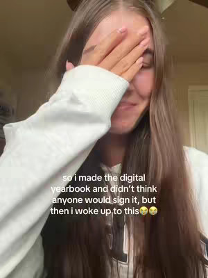 A young woman is shown in a selfie, with her right hand covering her eyes. She's wearing a white sweater. The background appears to be a warm-toned interior, possibly a room. Text overlayed on the image reads "so i made the digital yearbook and didn't think anyone would sign it, but then i woke up to this". The overall mood seems emotional, with the woman's expression hinting at surprise or happiness.