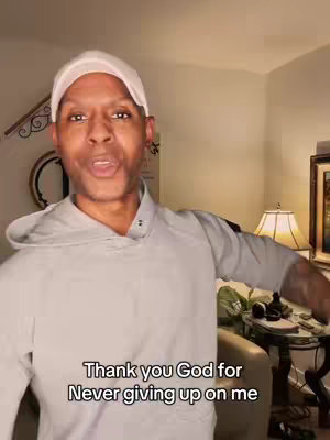 A man wearing a white cap and a gray hoodie is in a room. The text overlay indicates "Thank you God for Never giving up on me."