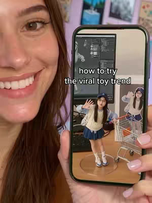 A woman with brown hair and visible teeth is holding a phone that displays a screen showing a woman in a miniature, figurine-like form posing on a round platform next to a shopping cart. The woman holding the phone is smiling, and the background includes a cluttered room with a purple shelf and framed pictures.