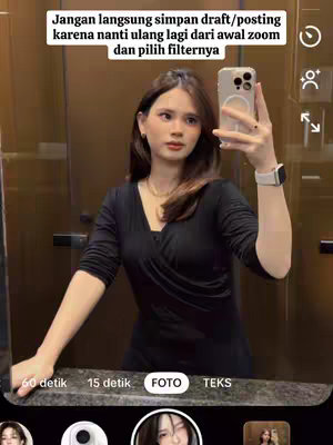 A woman is taking a selfie in front of a mirror. She's wearing a black top and has a watch on her wrist. The mirror reflects the surroundings. There's text overlaying the image in Indonesian.