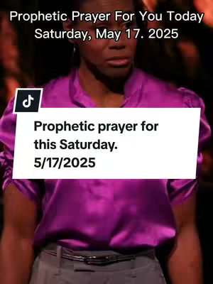 A medium shot features a woman of color with short hair, wearing a purple satin blouse and gray pants. The background is out of focus, with the TikTok logo on the left side and text overlayed on the image. The woman has a serious expression, looking off to the side. The text overlay has the title: Prophetic prayer for this Saturday. 5/17/2025.