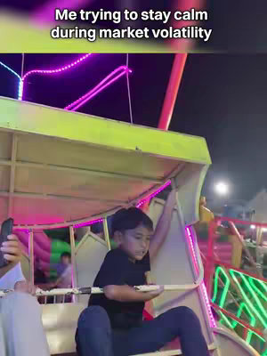 A boy is sitting in a carnival ride with neon lights visible.  Text overlay says,"Me trying to stay calm during market volatility".