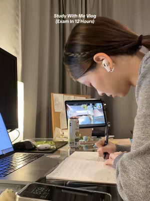 A well-lit photo shows a young woman studying at a desk. She is writing in a notebook, with a laptop and phone nearby. A can of Celsius energy drink sits on the desk. The background is softly blurred, suggesting a home study environment.