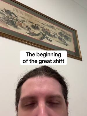 The cover image shows a man's face from the chest up, with his eyes closed. Above him, there is a framed painting in the background. A rectangular text overlay towards the bottom of the painting reads, "The beginning of the great shift".