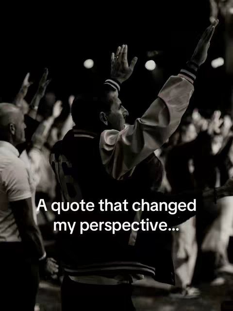 A black and white photo of a group of people with their arms raised in the air. In the foreground, a man is raising his arms high, and the camera focuses on him. The background is dark, but it looks like a crowd with blurred figures. White text is visible at the bottom of the image.