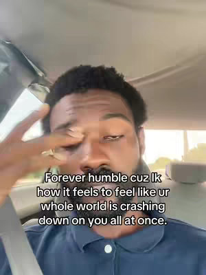 A close-up shot of a Black man inside a car. He is looking towards the viewer with a somber expression, hand raised near his eye. Text overlay indicates this is a selfie.
