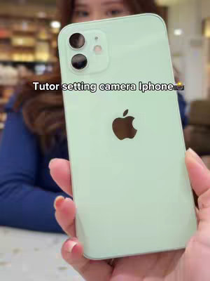 The cover image shows a light green iPhone held up in front of a blurred background. The phone is the central focus, with the Apple logo clearly visible. The person holding the phone is visible only from the chest up, and they have fair skin and are wearing a blue shirt. The background has a warm, blurry indoor setting.