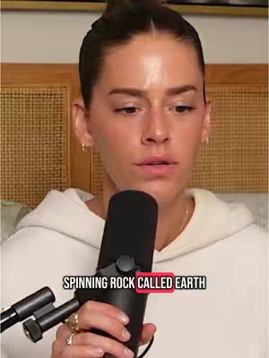 A woman with dark hair styled back is positioned in front of a microphone, looking slightly to the side while speaking. The background has a light wooden panel and a beige upholstered surface, suggesting a casual setting like a podcast studio. A text overlay at the bottom of the image reads "Spinning Rock Called Earth", with the word "Earth" highlighted in red.