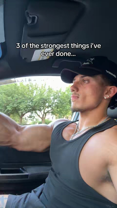 A man is sitting in a car, seen from the driver's seat. He is wearing a black tank top and a black cap. The background shows trees and a daytime setting. Text overlay reads '3 of the strongest things i've ever done...'