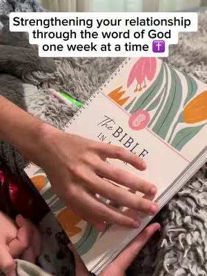 The image shows a person holding a Bible with both hands, open. The book is open, revealing the pages. The background is out of focus, which appears to be a bedspread. Text overlays at the top.