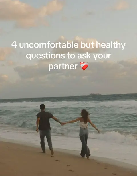 A couple walking along the beach, holding hands, as a body of water washes the shore nearby.