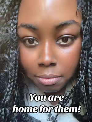 A close-up shot focuses on a Black woman's face, framed by braided hair. She has a neutral expression. The background is intentionally blurred, emphasizing the woman's features.