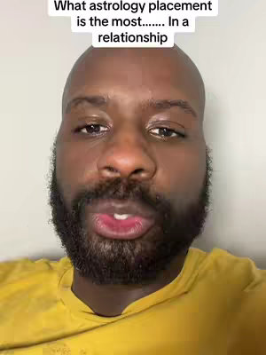 A close-up shot of a Black man with a bald head and a full beard. The man is wearing a yellow shirt and is looking directly at the camera with his mouth slightly open, as if speaking. Overlayed text is visible towards the top of the image.