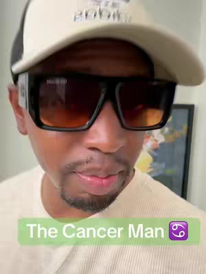 A close-up shot of a Black man wearing a white cap, large black sunglasses, and a white t-shirt. A green rectangle at the bottom reads 'The Cancer Man' with a Cancer zodiac symbol.