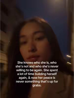 A woman is centered in the frame, with soft lighting casting a warm glow on her face. She has long dark hair that partially obscures the upper half of her face. Text is overlaid on the image using a white font. The background is blurred, but suggests an outdoor setting with dark sky and streetlights.