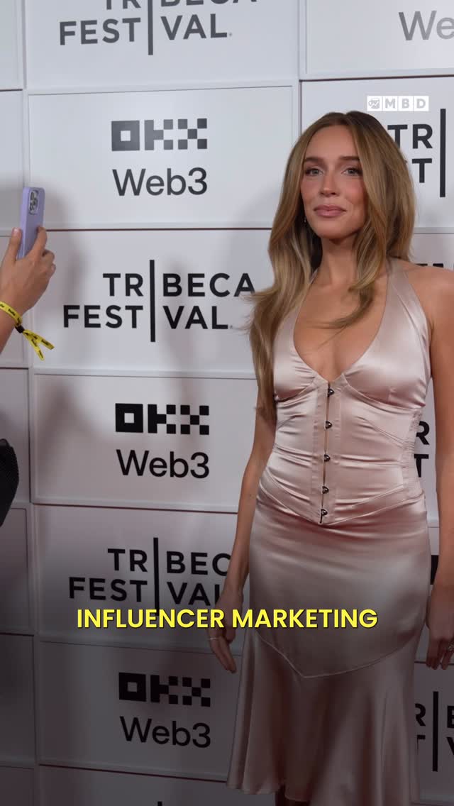 A woman in a silk dress stands in front of a backdrop with the Tribeca Film Festival logo. A person on the left is holding a phone to capture the image. The hook "Influencer Marketing" is displayed in a yellow box at the bottom.