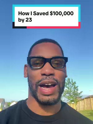 A man with dark skin and a short beard wearing square black glasses is smiling and looking slightly down at the camera against a backdrop of a blue sky and some greenery. Directly above the person's head, there's a rectangular text box with the words 'How I Saved $100,000 by 23'.