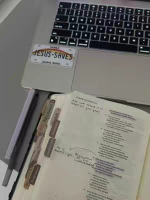 The cover image shows a close-up of a laptop with a sticker on it and a Bible open to a marked page. The laptop is silver, and the sticker says "Jesus Saves". The Bible has various tabs and handwritten notes with the page spread visible. The color scheme is primarily neutral with a focus on the text and the items placed around.