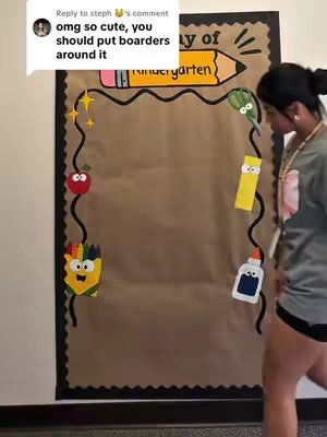 A woman stands beside a bulletin board that is decorated with school-themed cutouts, such as a pencil, apple, and glue bottle.