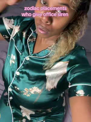 A woman is shown from the chest up, looking directly into the camera with a slightly open mouth. She is wearing a dark green silky pajama set with white accents. The background is a blur of a soft gray.